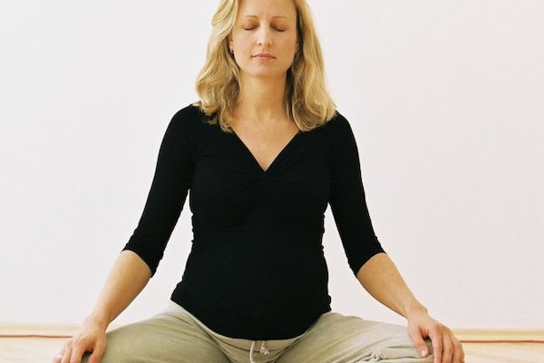 Meditation - Schwangere Frau meditiert mit verschränkten Beinen im DAO Zentrum