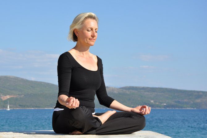 Sabine Barta meditierend am Strand mit blauem Himmel