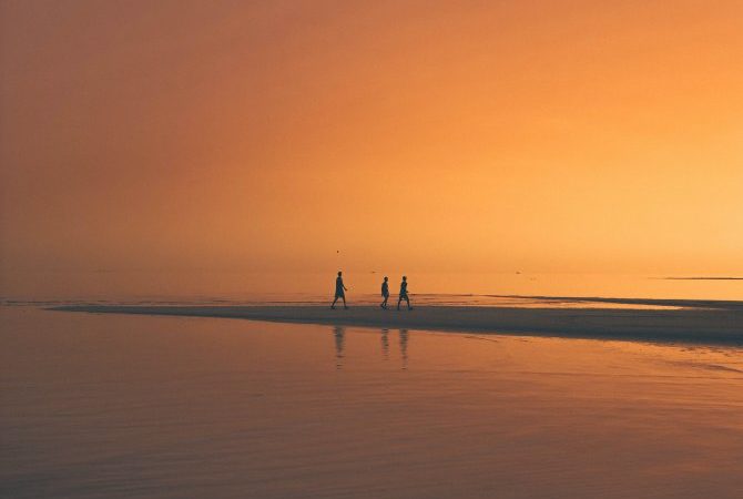 Drei Personen am einsamen Strand im Orangeton