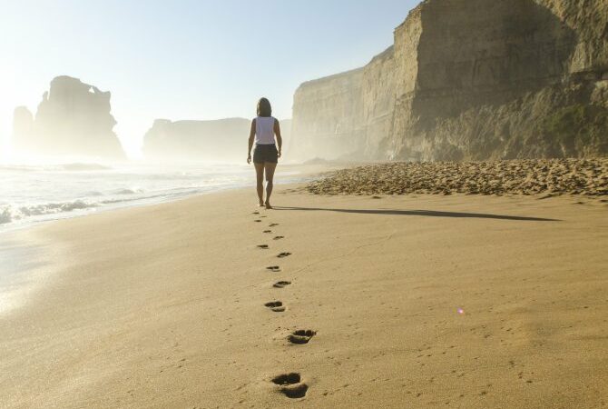 Gehmeditation, Frau von hinten, geht am Strand entlang, Fußspuren im Sand